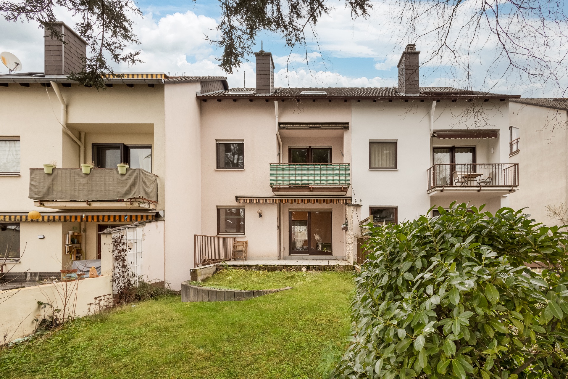 Rückansicht eines mehrstöckigen Wohnhauses mit Balkon, Terrasse und kleinem Garten.