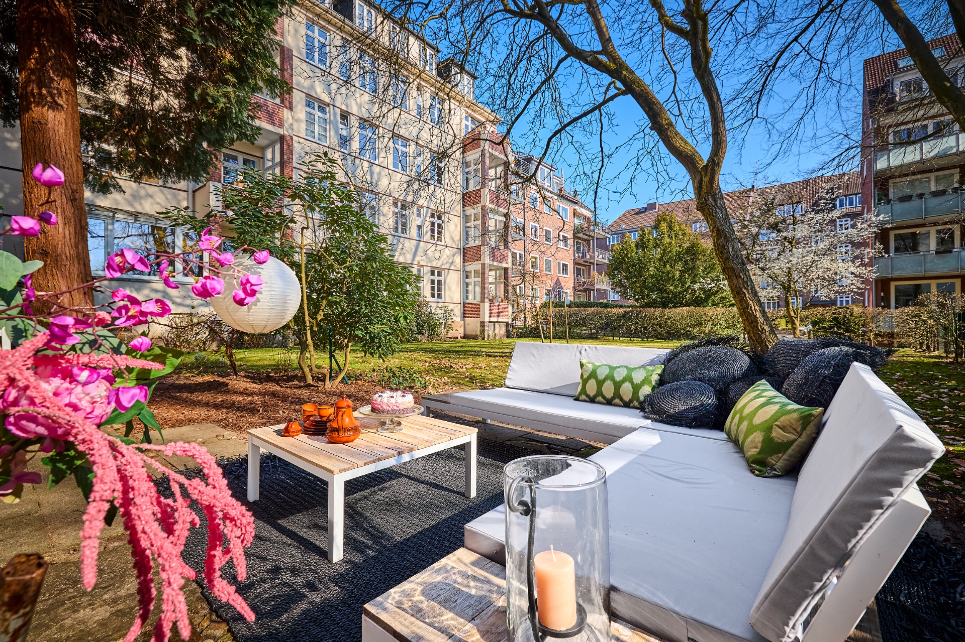 Gemütliche Sitzgruppe mit Kissen und Tisch im Garten eines Wohnhauses bei sonnigem Wetter.