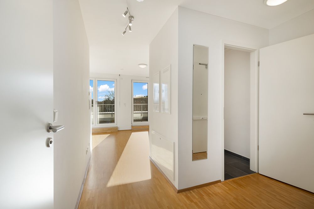 Heller Flur mit Holzfußboden, weißen Wänden und Zugang zu Balkon sowie offenem Zimmer.