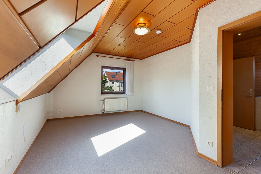 Helles Zimmer mit Dachschräge, Fenster, Heizkörper und Holzdecke in einer Wohnung.
