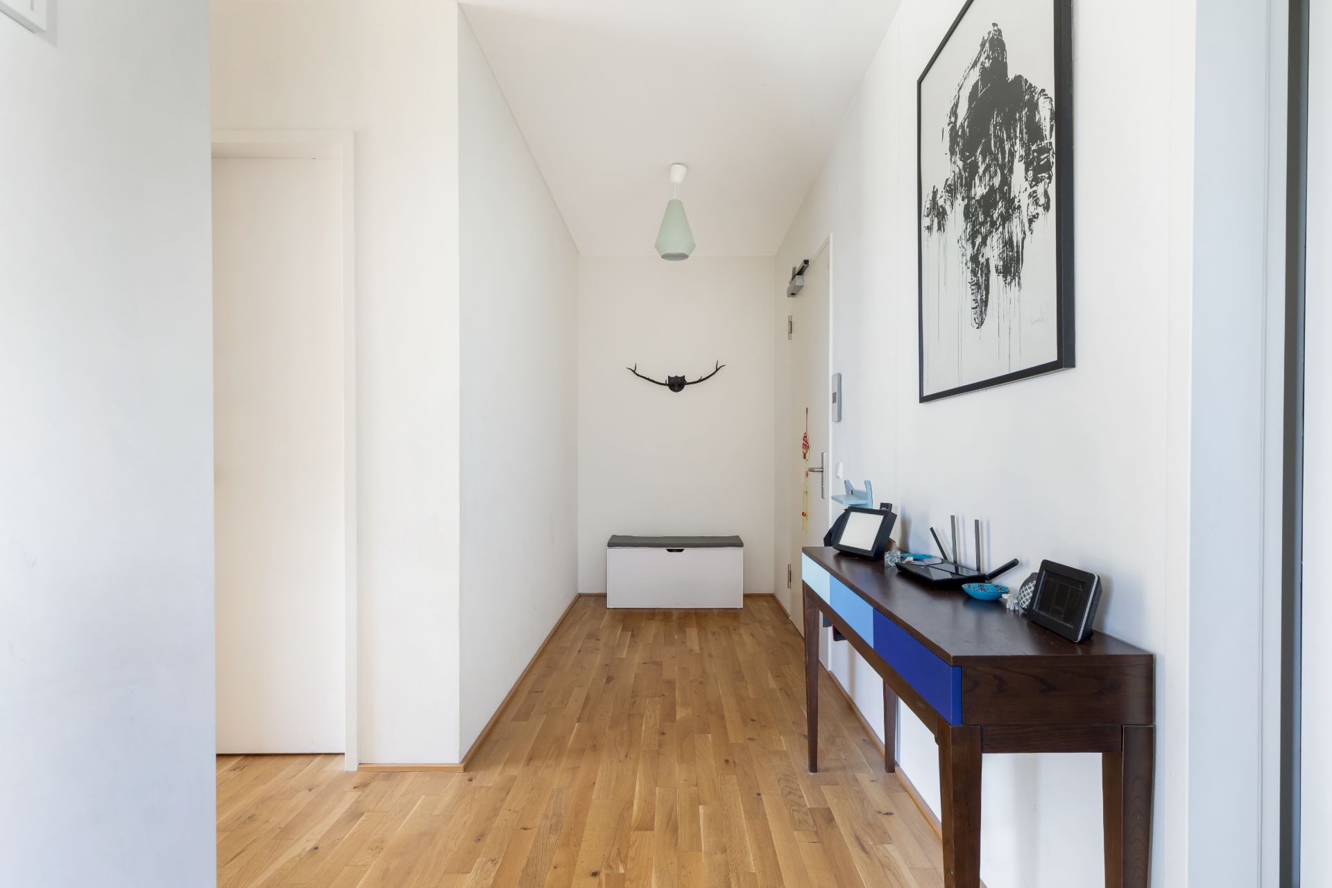 Heller Flur mit Holzfußboden, Kommode, Sitztruhe und Wandbild.