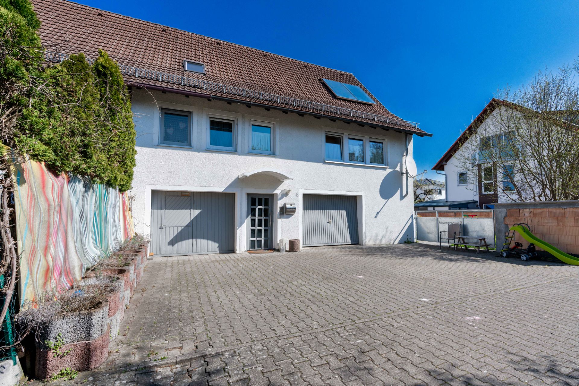 Zweistöckiges Wohnhaus mit zwei Garagen und gepflastertem Hof, Rutsche im rechten Bereich.