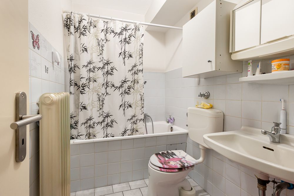 Kleines Badezimmer mit Badewanne, Duschvorhang, Toilette und Waschbecken.