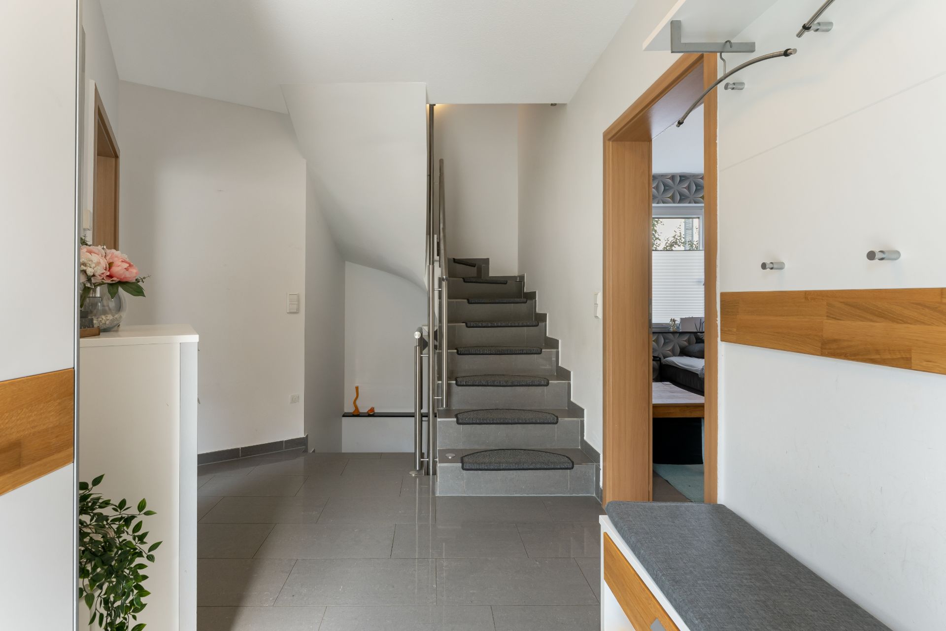Heller Flur mit Treppe, Kleiderhaken, Sitzbank und Zugang zu einem weiteren Raum.