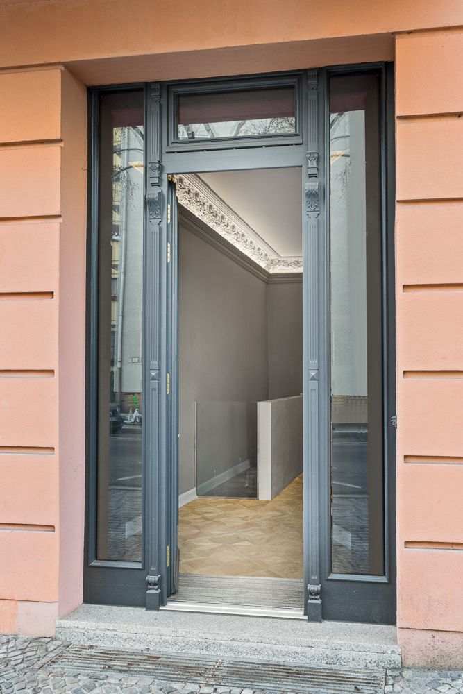 Offene Glastür an einer Hausfassade mit Blick auf einen Flur und verzierten Stuck an der Decke.