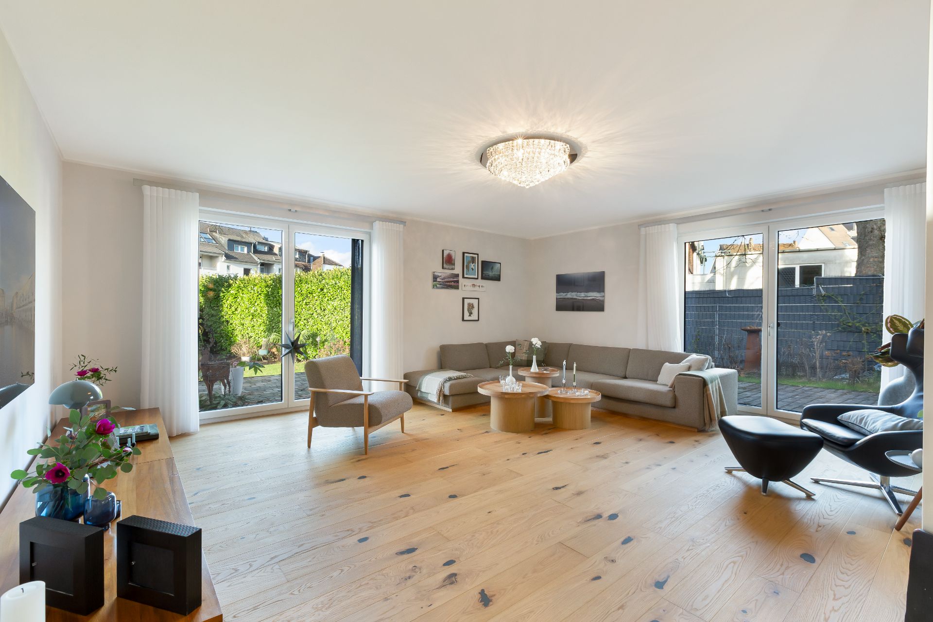 Helles Wohnzimmer mit Holzboden, Sofa, Sesseln, Couchtisch und großen Fenstern zum Garten.