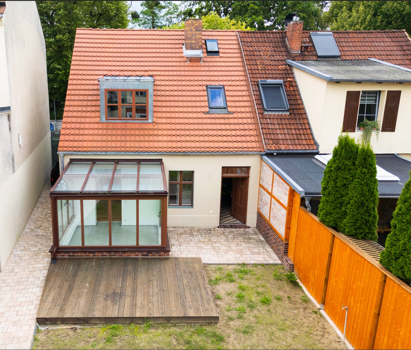 Rückansicht eines Hauses mit Wintergarten, Holzterrasse und kleinem Gartenbereich.