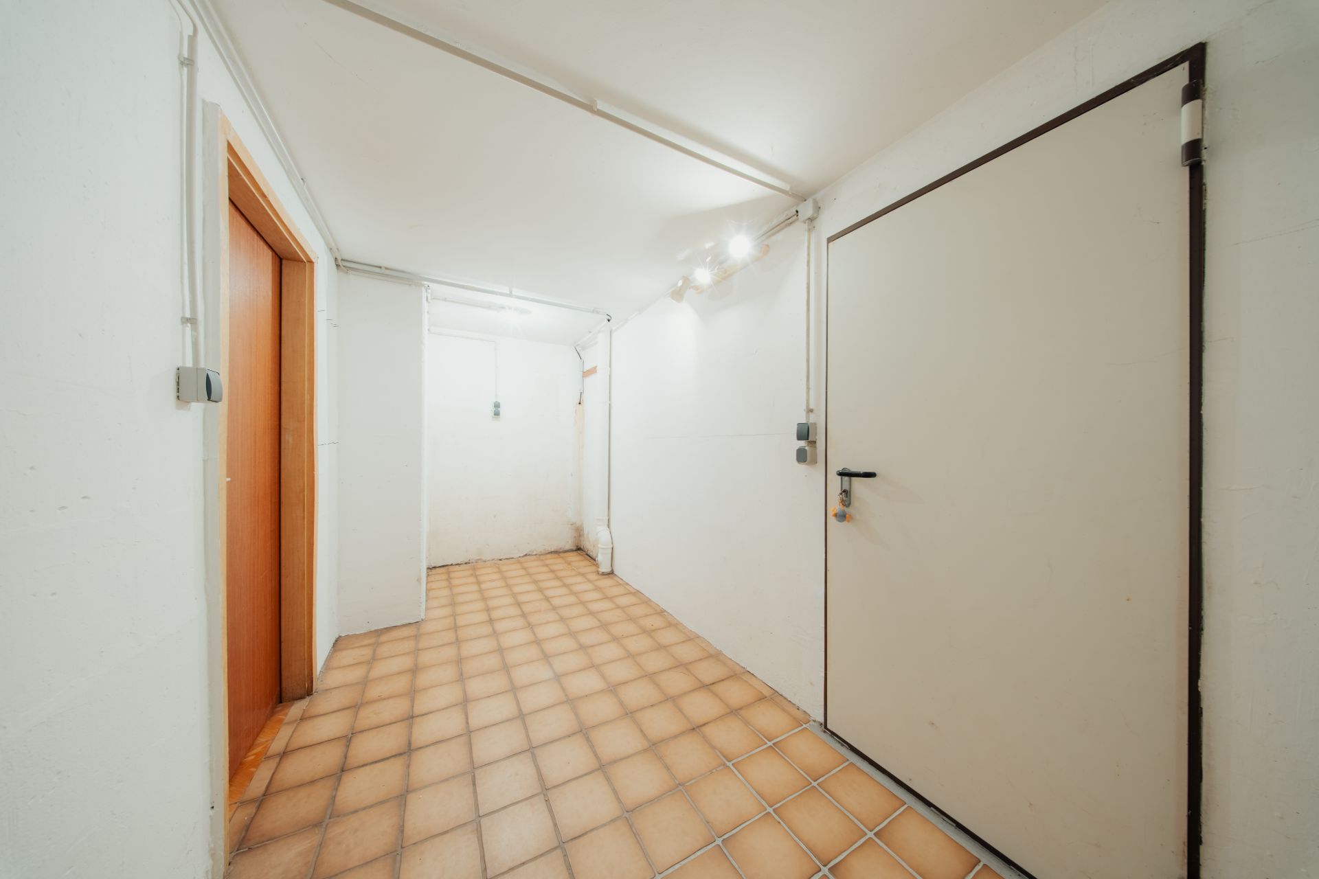 Heller Flur mit Fliesenboden, weißen Wänden und zwei Türen in einem Wohngebäude.