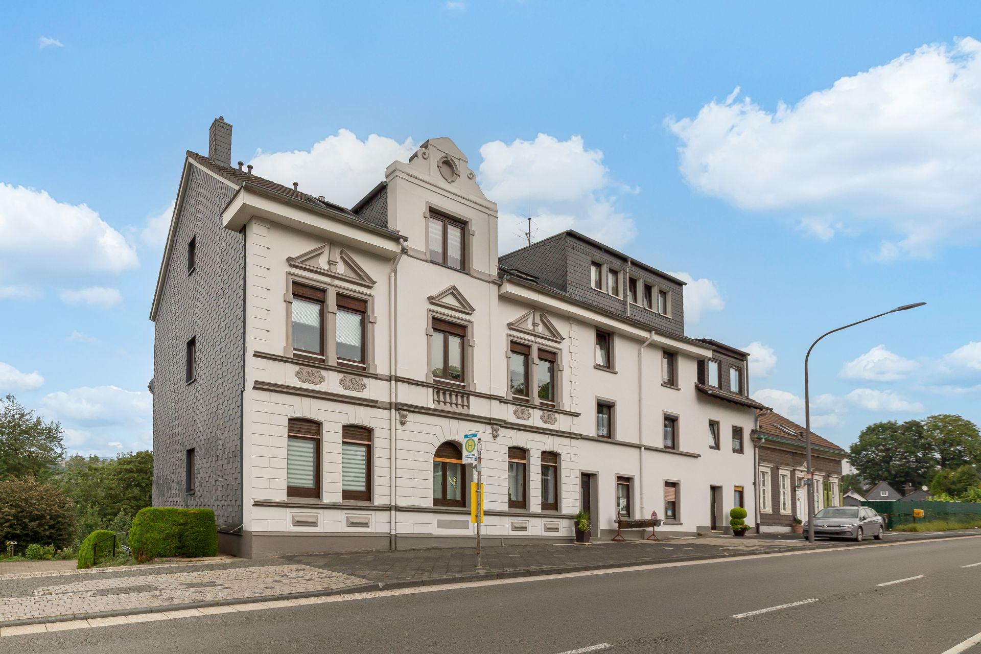 Großes weißes Wohnhaus mit architektonischen Details an einer Straße bei Tageslicht.