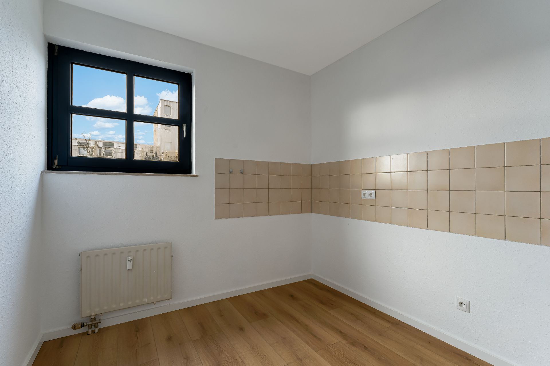 Leerer Raum mit Holzboden, Fliesen an der Wand, Fenster und Heizkörper.