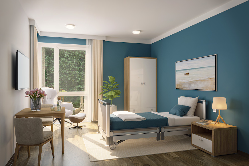 Helles Schlafzimmer mit Pflegebett, Schrank, Nachttisch, Schreibtisch und Sessel vor großem Fenster.