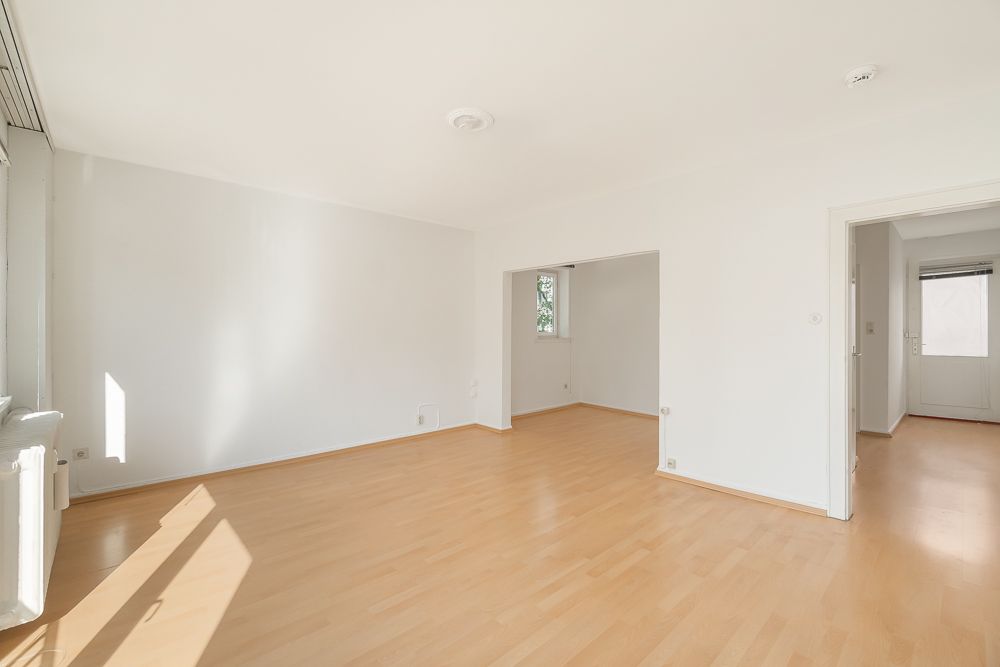Helles, leeres Zimmer mit Holzfußboden und weißen Wänden, Türen zu weiteren Räumen sichtbar.