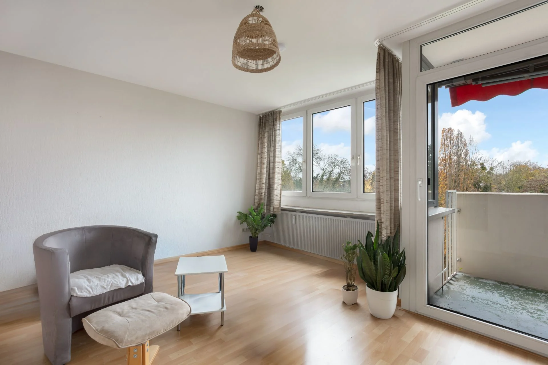 Helles Wohnzimmer mit Sessel, Fußhocker, kleinem Tisch, Pflanzen und Zugang zum Balkon.