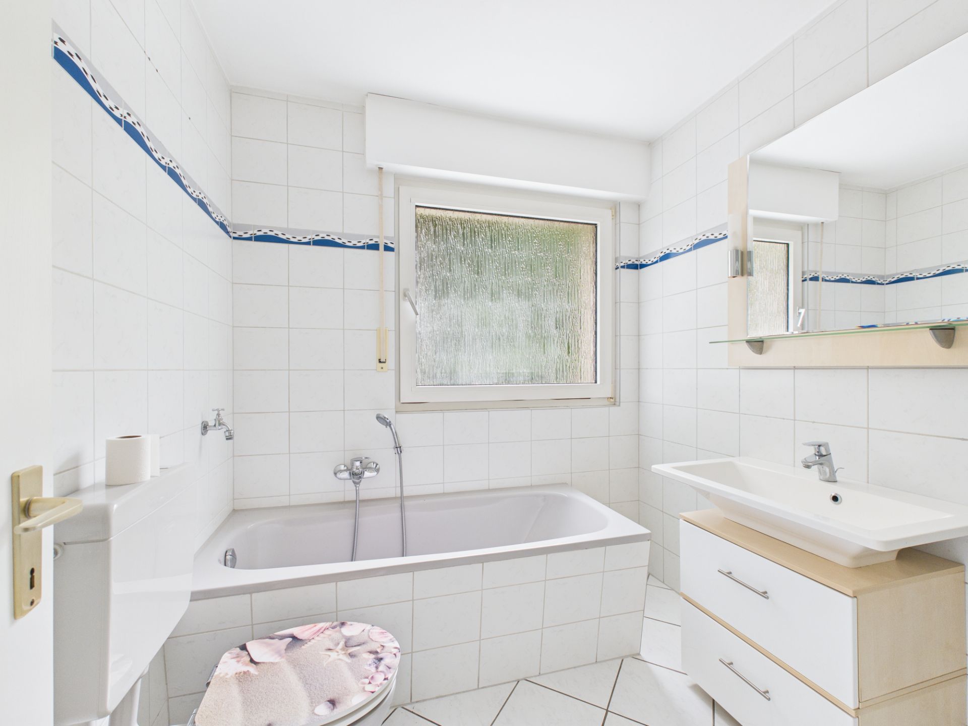 Helles Badezimmer mit Badewanne, Waschbecken, Spiegel, WC und Fenster.