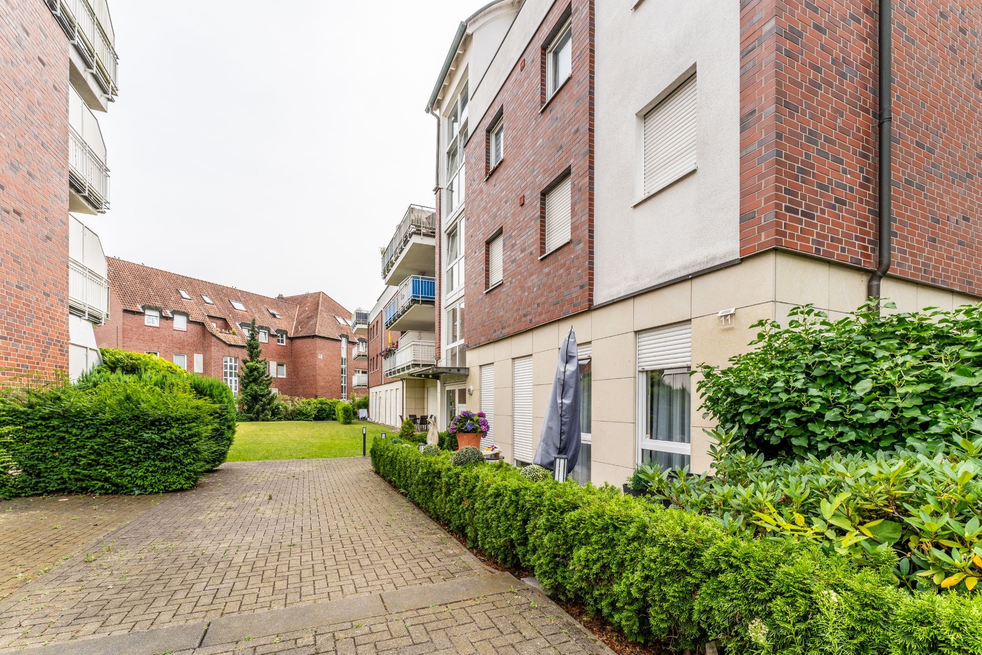 Gepflegter Innenhof mit Grünfläche, Hecken und mehrstöckigem Wohnhaus aus Klinker.