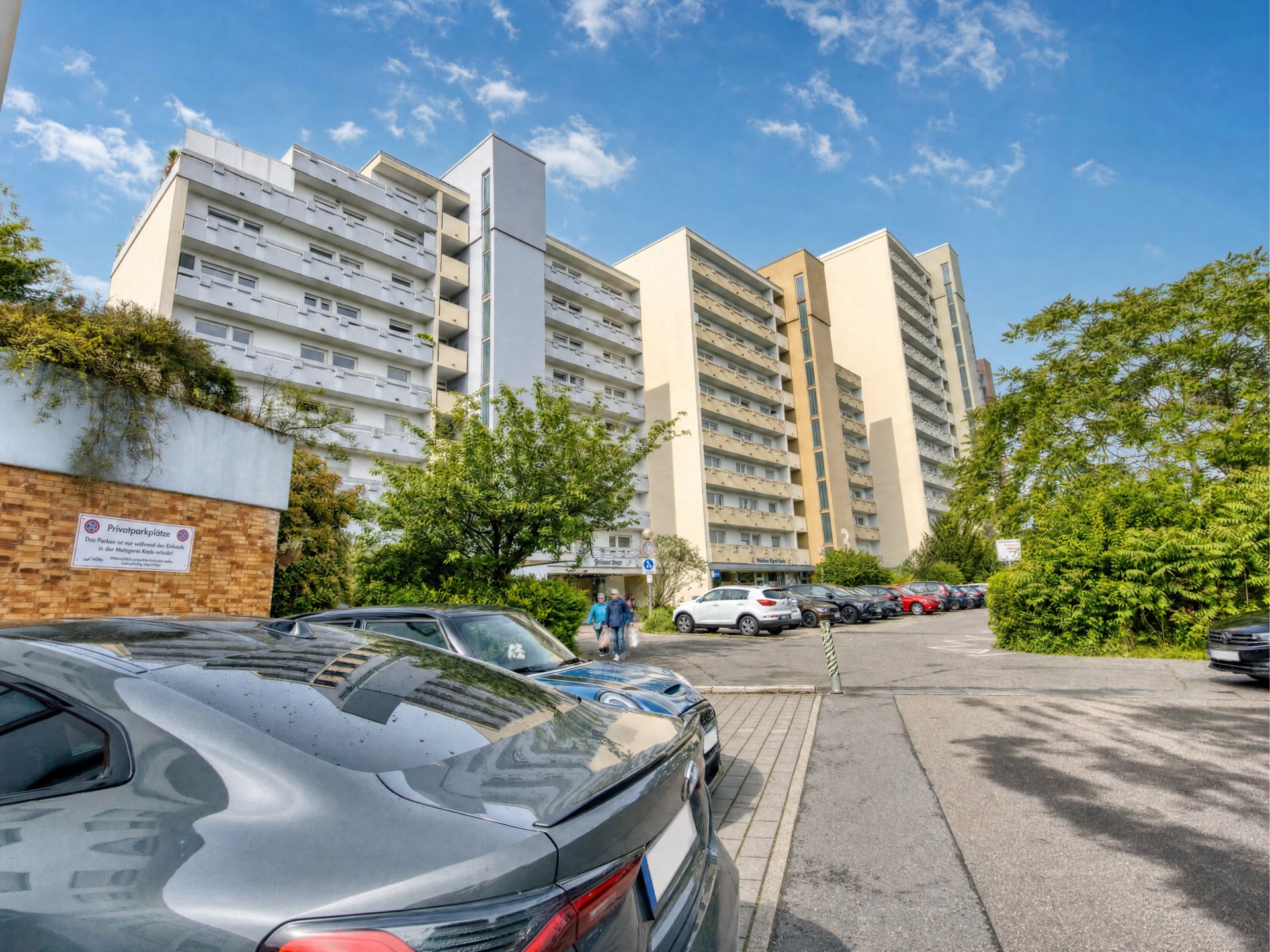Mehrstöckiges Wohngebäude mit Parkplatz und Autos im Vordergrund.