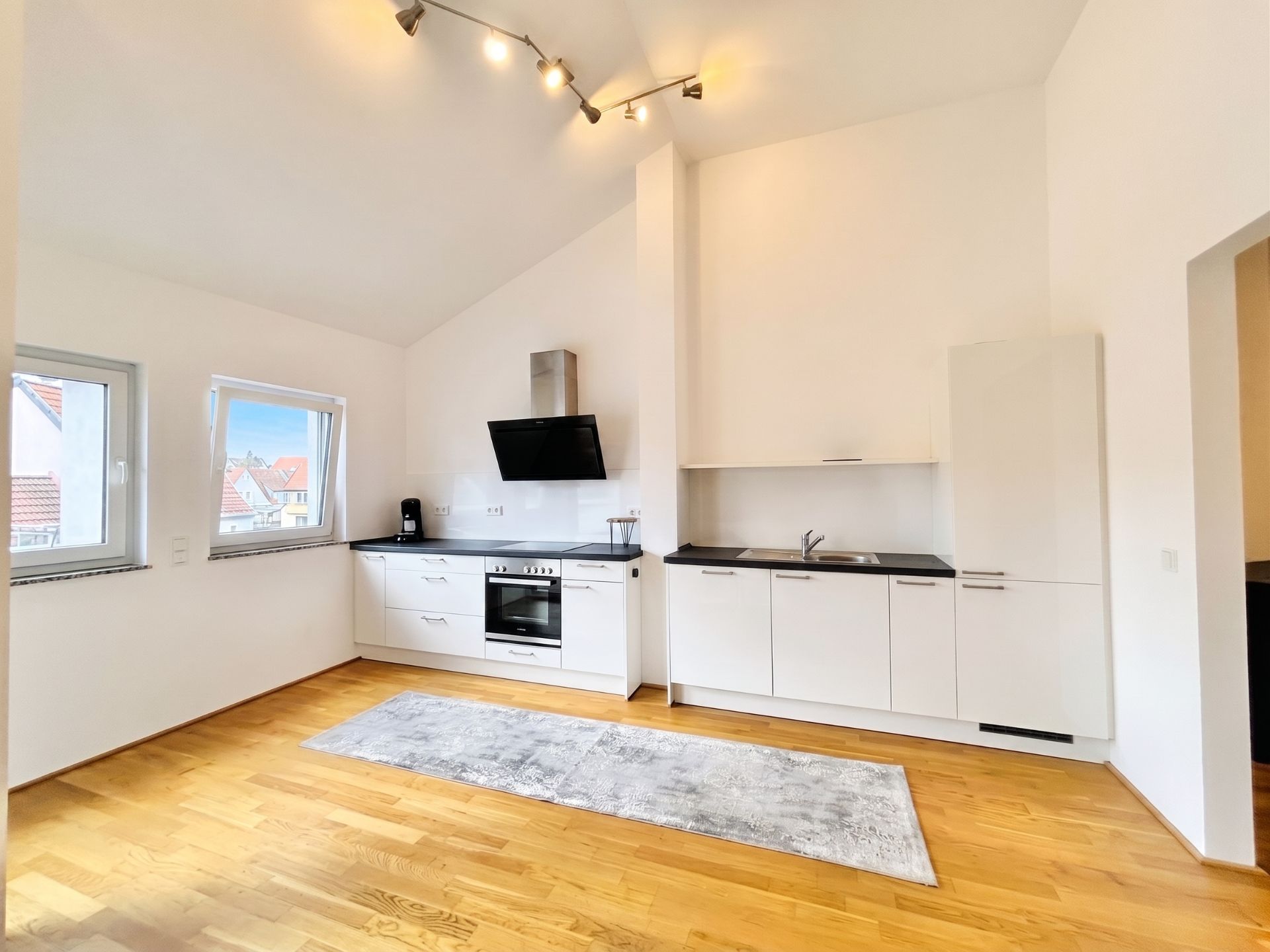 Moderne Einbauküche mit weißen Schränken, Holzfußboden und zwei Fenstern.