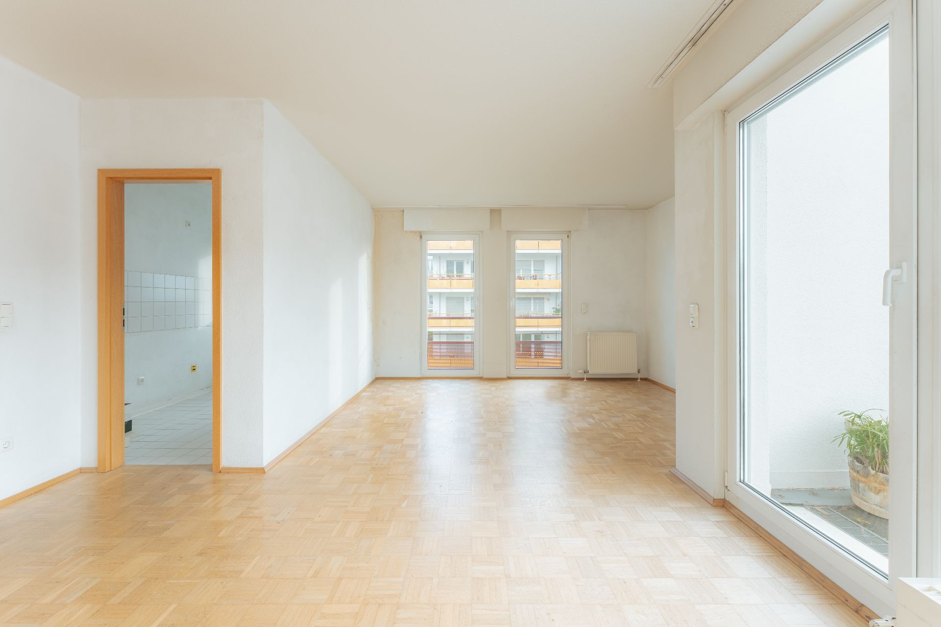 Helles Wohnzimmer mit Parkettboden, großen Fenstern und Zugang zu einem Balkon.