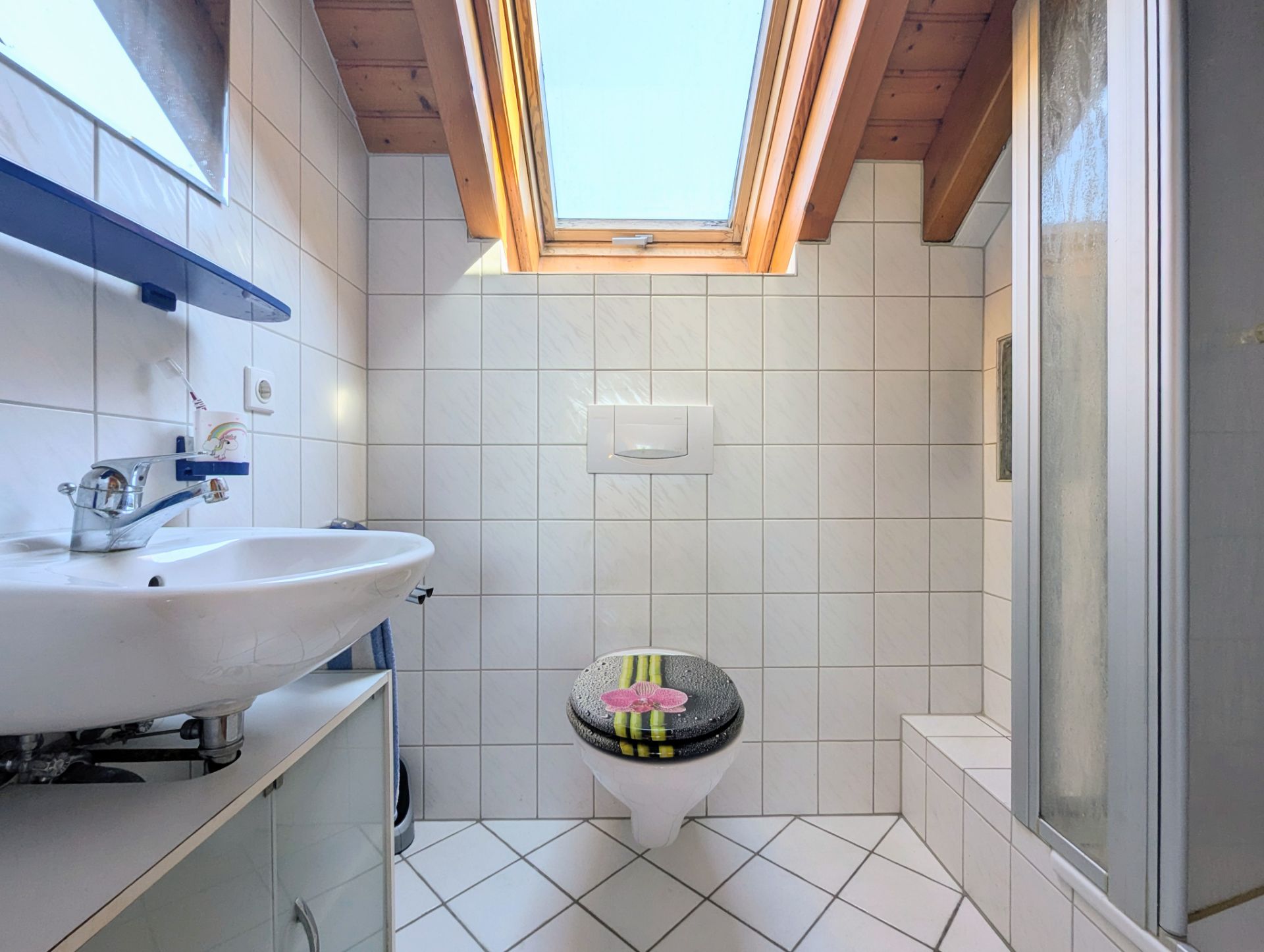 Helles Badezimmer mit Dachfenster, Waschbecken, Toilette und Dusche mit Glaswand.
