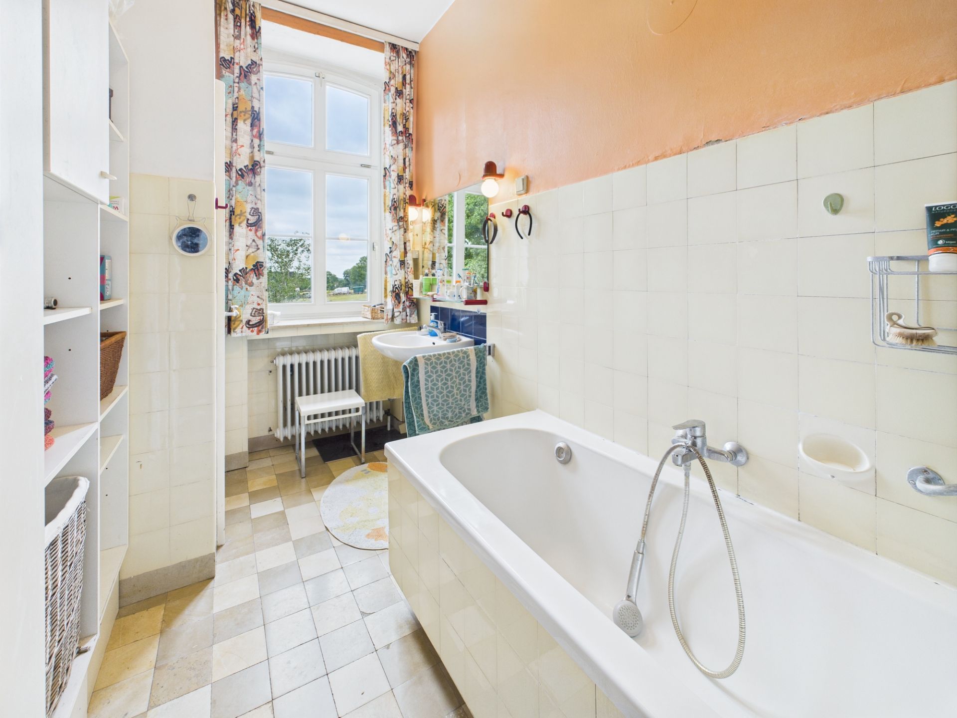 Helles Badezimmer mit Badewanne, Waschbecken, Fenster und Regal.