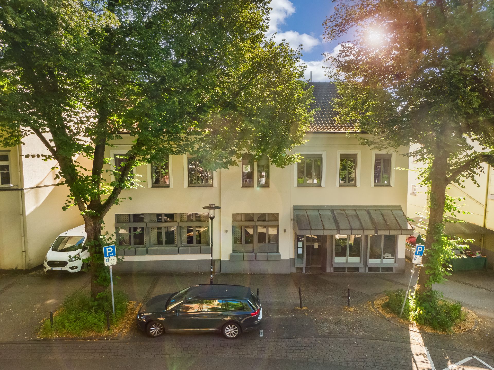 Zweistöckiges Wohnhaus mit großen Fenstern und zwei geparkten Autos vor dem Gebäude.