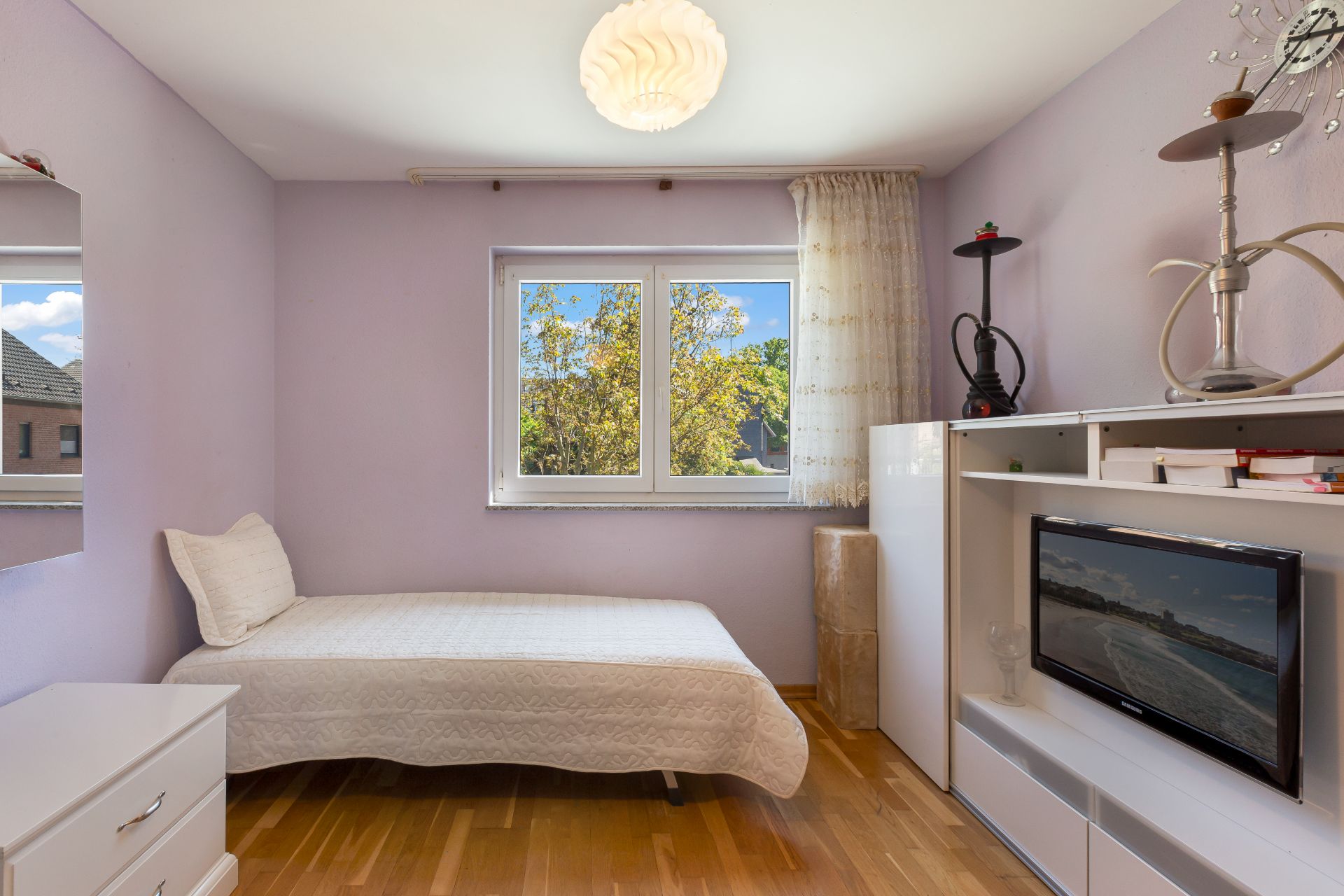 Helles Schlafzimmer mit Einzelbett, Fernseher und Regal, Holzboden und Fenster mit Blick nach draußen.