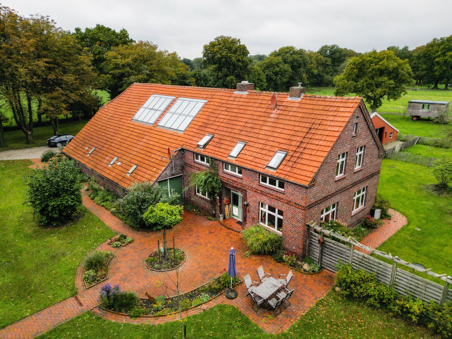 Backsteinhaus mit rotem Dach, großem Garten und Terrasse mit Sitzgruppe.