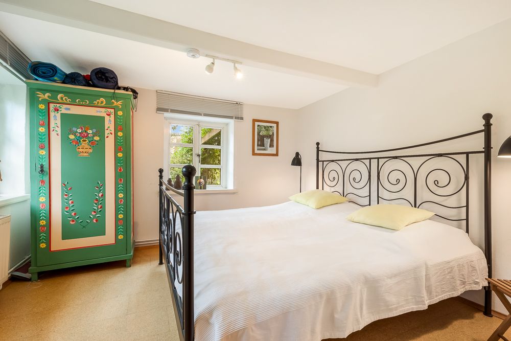 Schlafzimmer mit Doppelbett, grünem bemaltem Kleiderschrank und Fenster mit Blick ins Grüne.