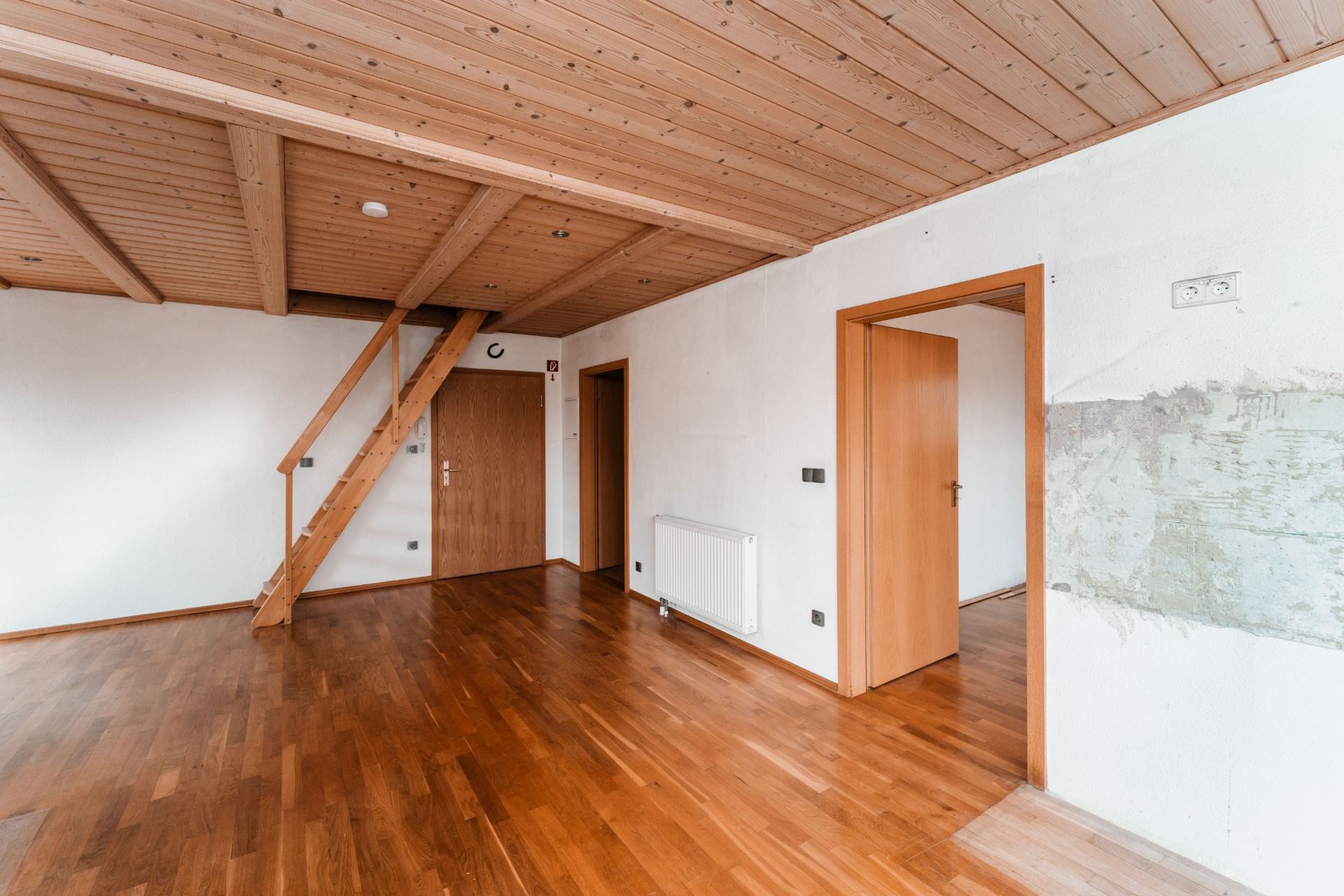 Leerer Raum mit Holzdecke, Parkettboden, Holztreppe und zwei offenen Türen.