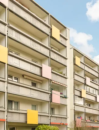 Mehrstöckiges Wohngebäude mit Balkonen und bunten Paneelen an den Geländern.