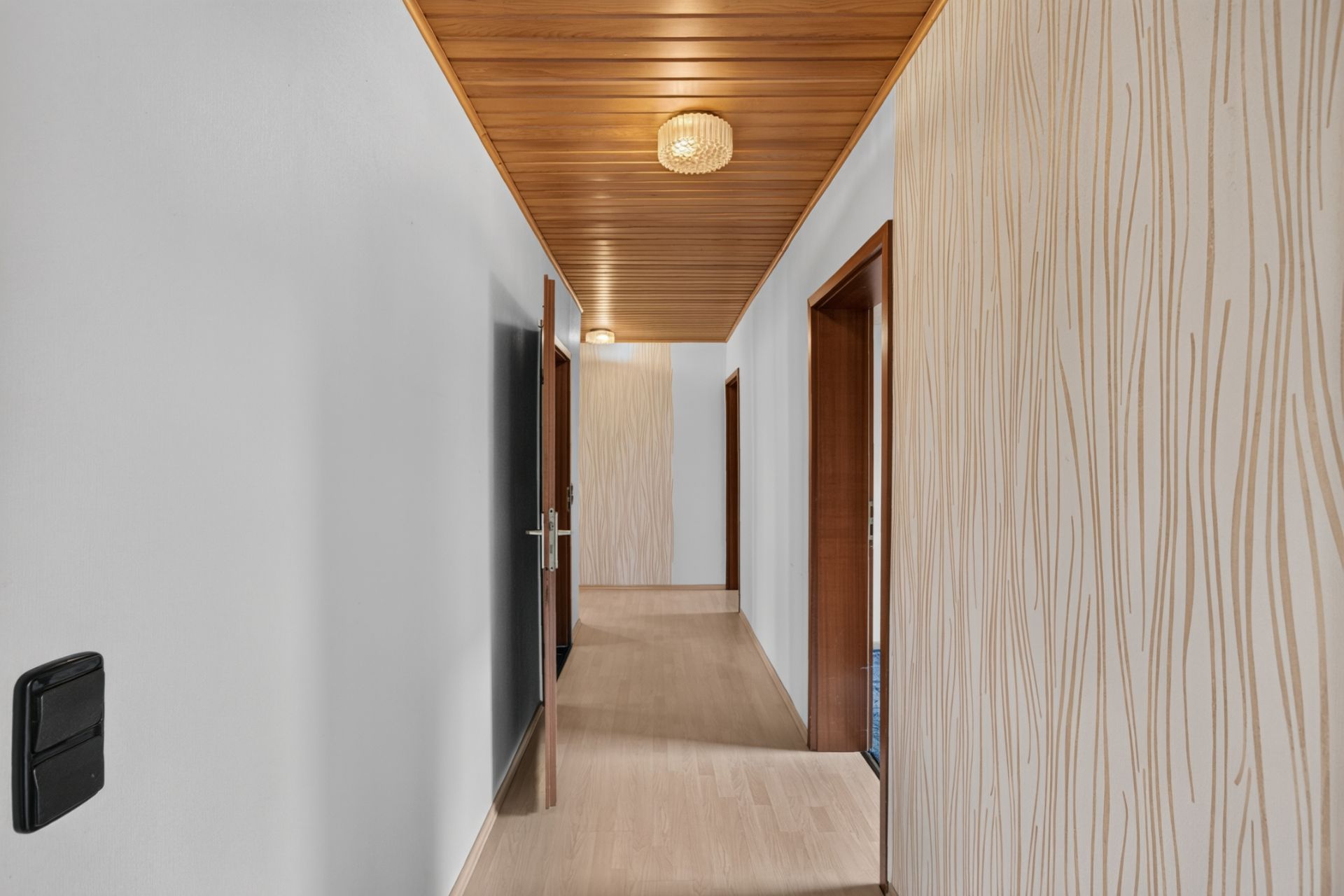 Heller Flur mit Holzboden, Holzdecke und gemusterter Tapete, mehrere Türen gehen ab.