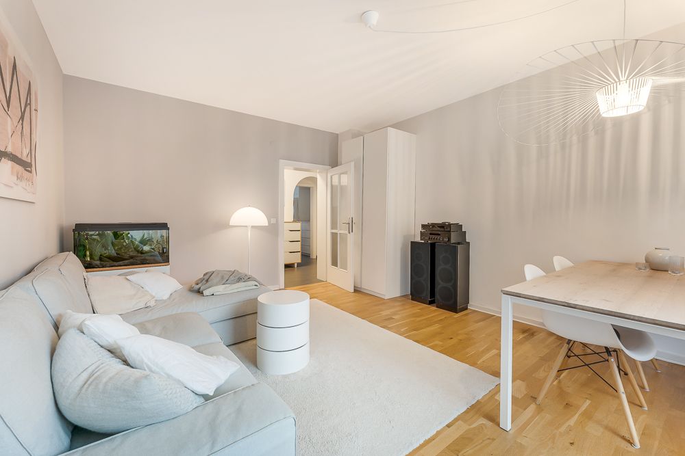 Helles Wohnzimmer mit Sofa, Aquarium, Esstisch, Stühlen und Stehlampe auf Holzfußboden.