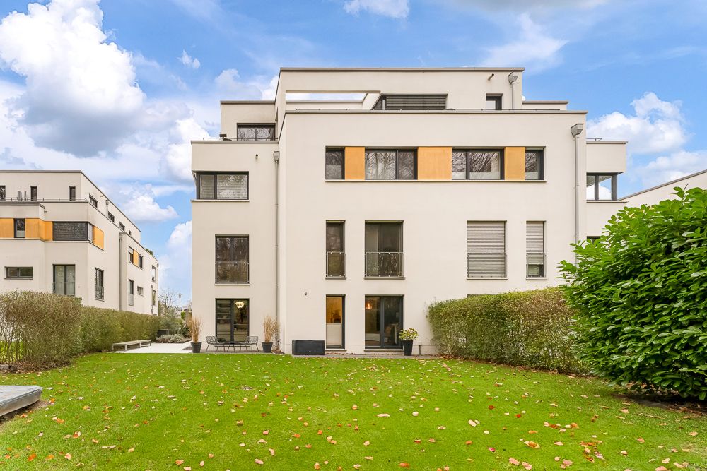 Moderne Wohngebäude mit weißer Fassade und großem grünen Garten im Vordergrund.