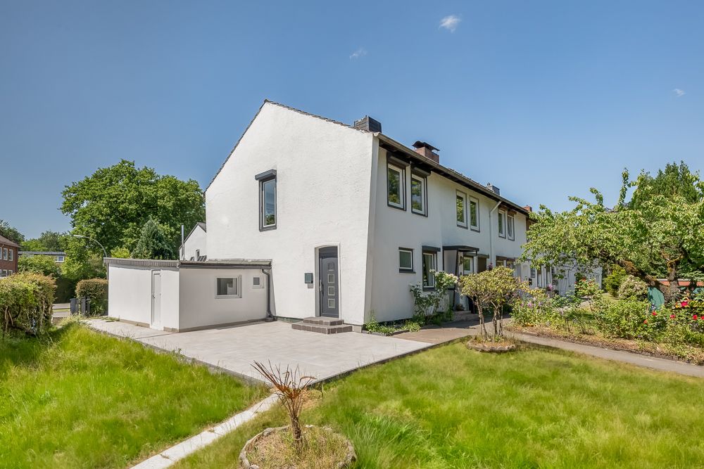 Weißes Reihenhaus mit Garten, Terrasse und Nebengebäude bei sonnigem Wetter.