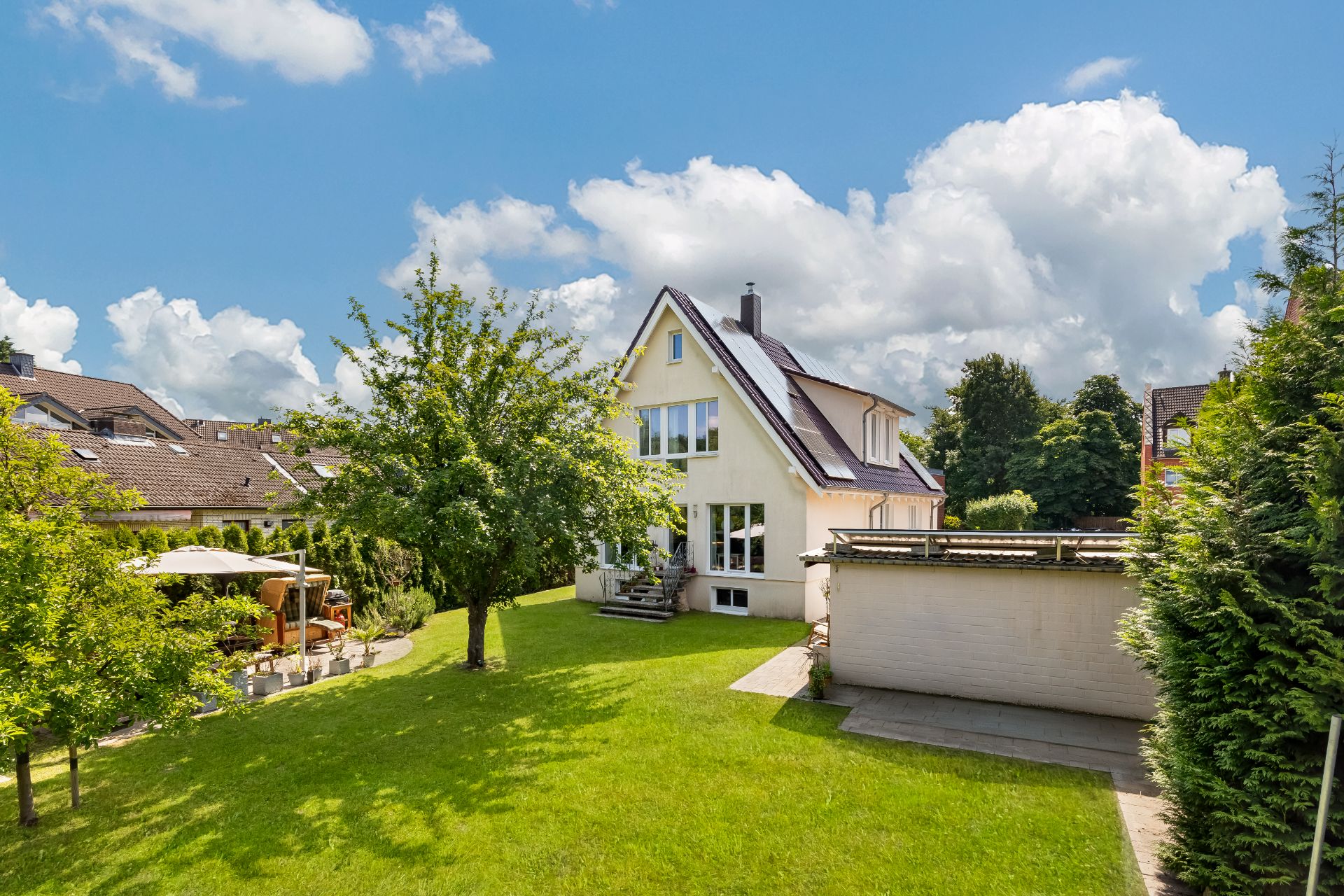 Einfamilienhaus mit großem Garten, Bäumen und Terrasse bei sonnigem Wetter.
