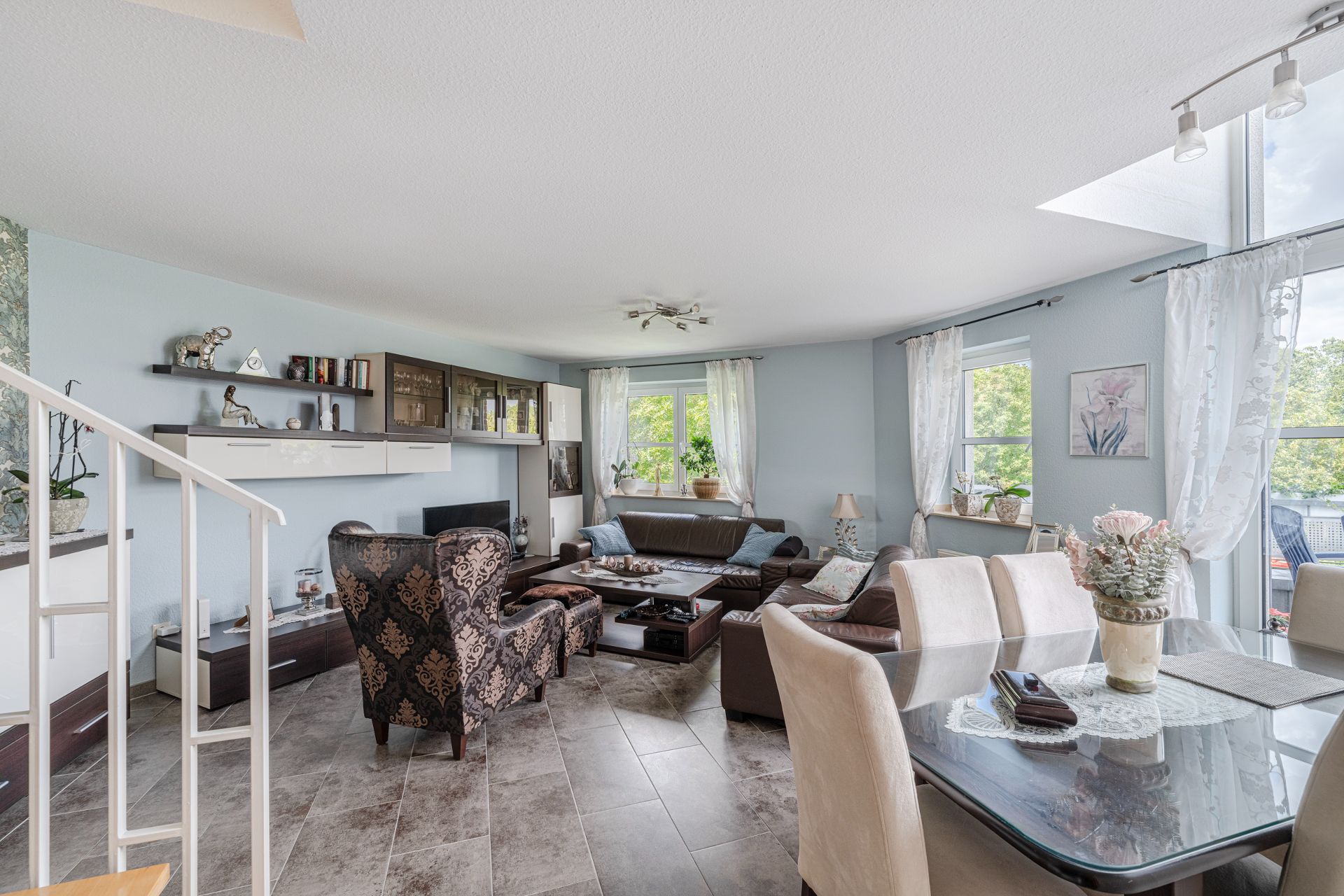 Helles Wohnzimmer mit Sofa, Sesseln, Esstisch und großen Fenstern mit Blick ins Grüne.