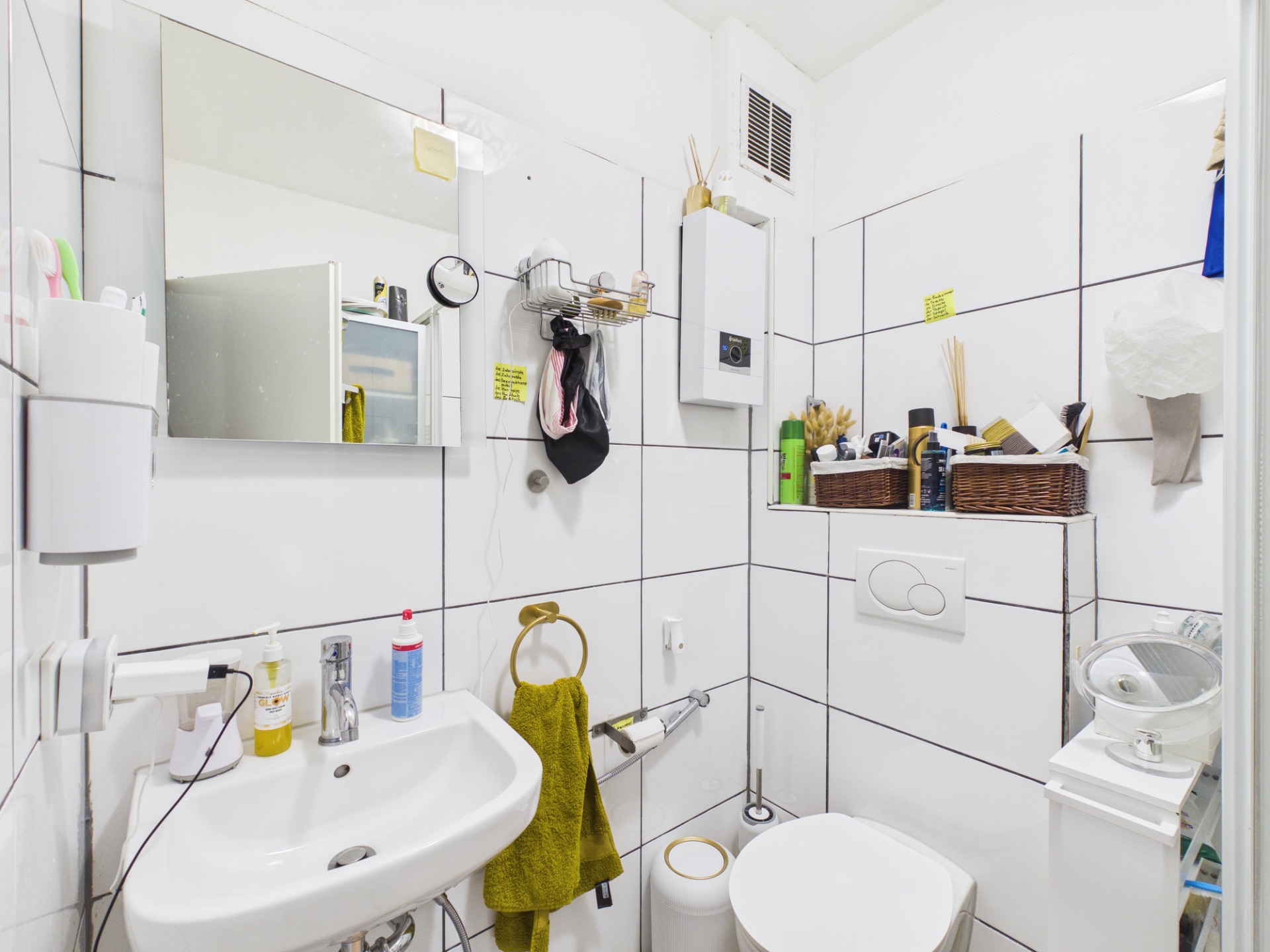 Kleines Badezimmer mit Waschbecken, Spiegel, Toilette und Regalen mit Toilettenartikeln.