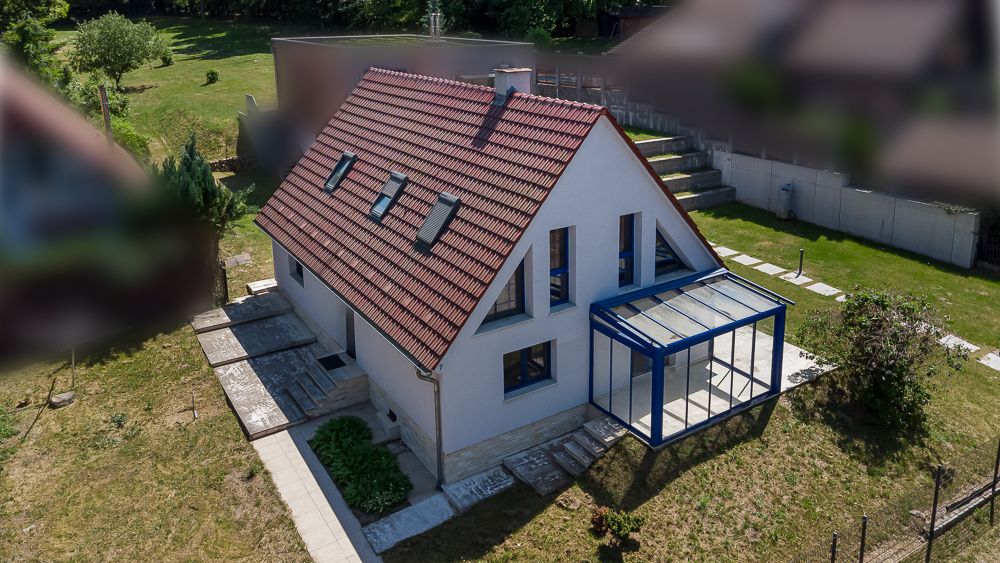 Einfamilienhaus mit rotem Satteldach, Wintergarten und Garten aus der Vogelperspektive.