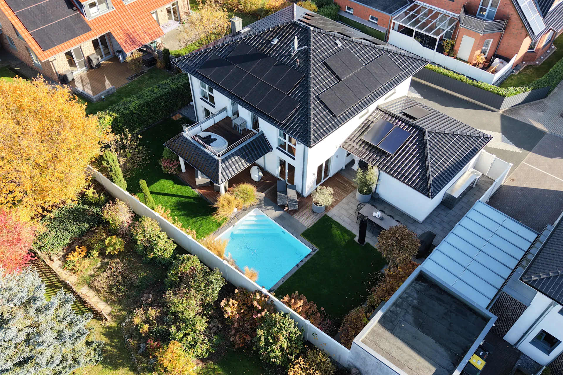 Moderne weiße Villa mit Pool im Garten, Photovoltaikanlagen auf dem Dach, umgeben von Bäumen und Hecken.