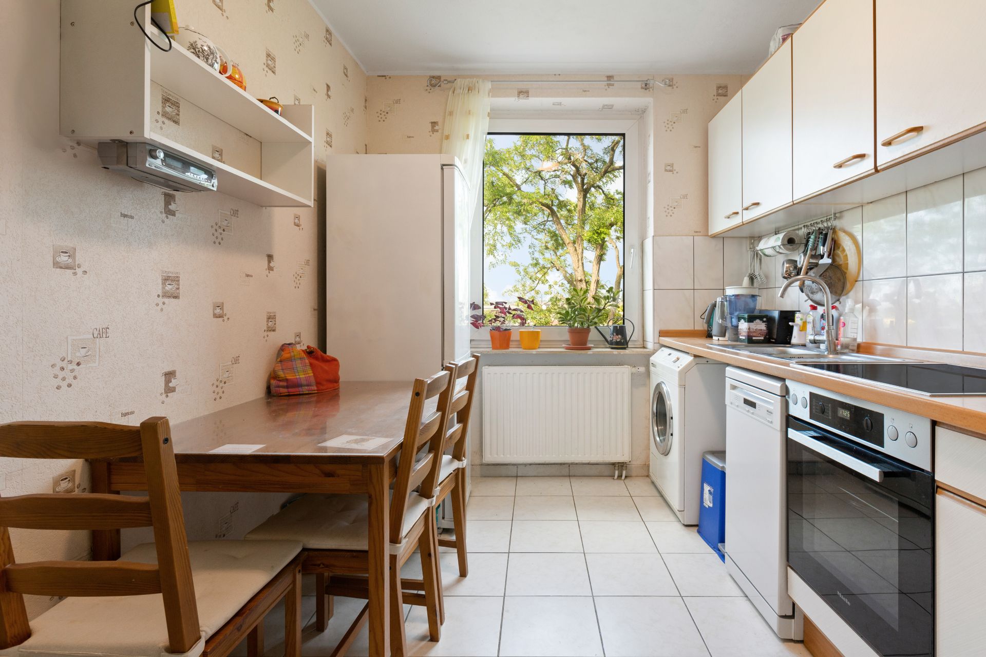 Küche mit Holztisch, vier Stühlen, Waschmaschine, Herd und Fenster mit Pflanzen.