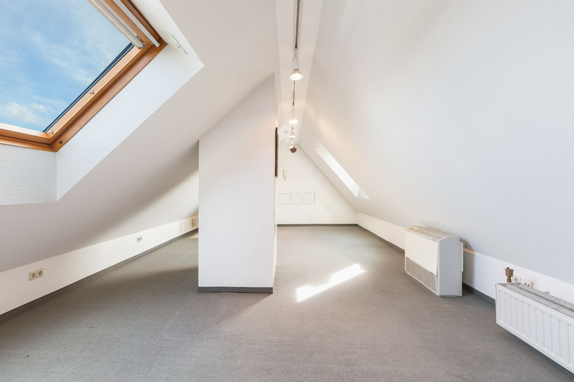 Heller Dachbodenraum mit Teppichboden, Dachfenstern und weißen Wänden.