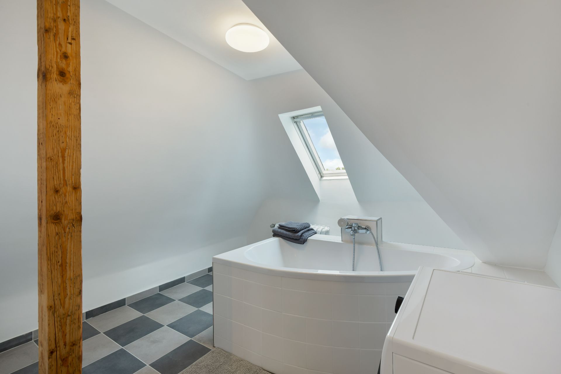 Modernes Bad mit Eckbadewanne, Dachfenster und Waschmaschine unter einer Dachschräge.