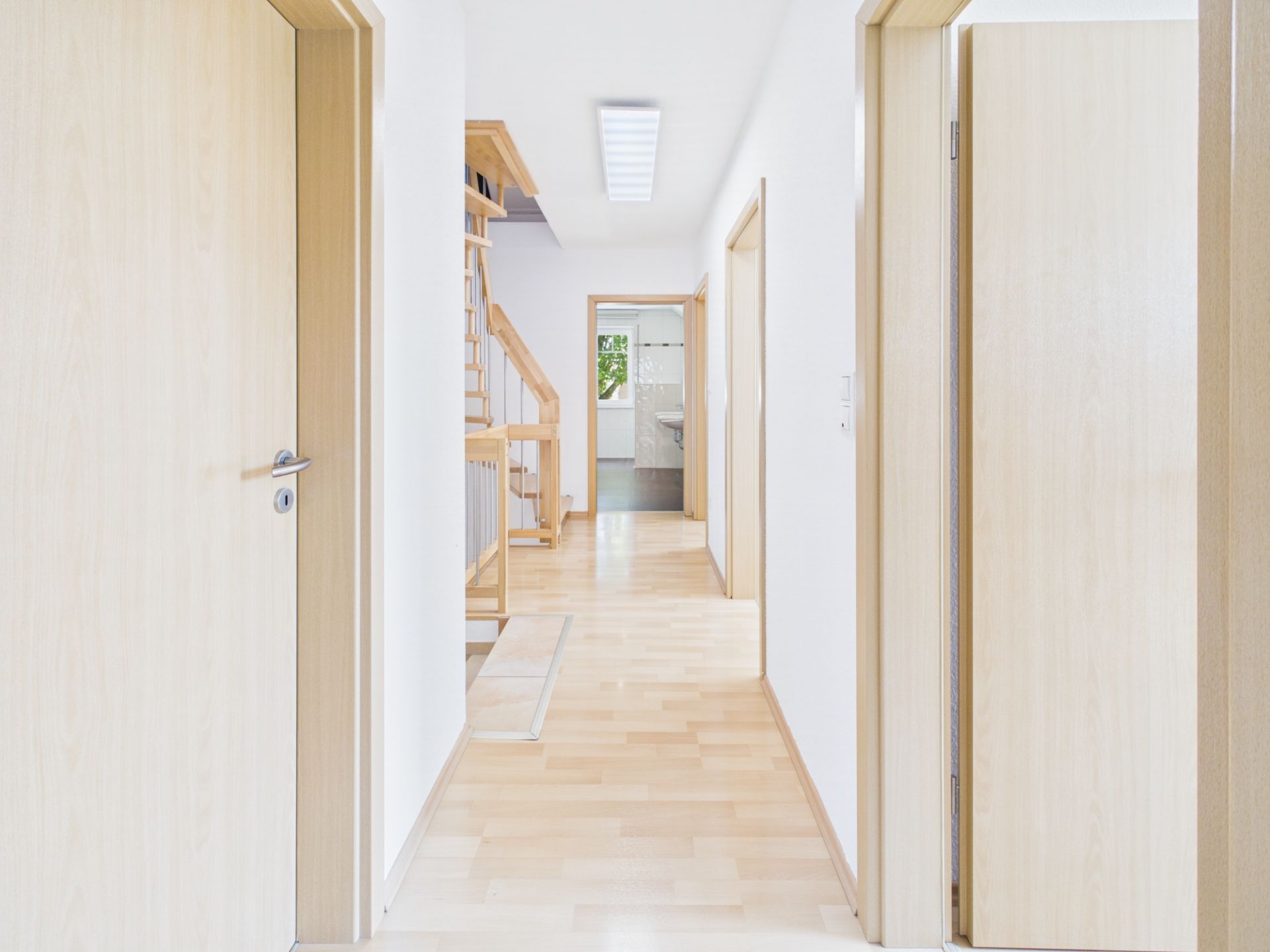 Heller Flur mit Holztüren, Parkettboden und Treppe im Hintergrund.