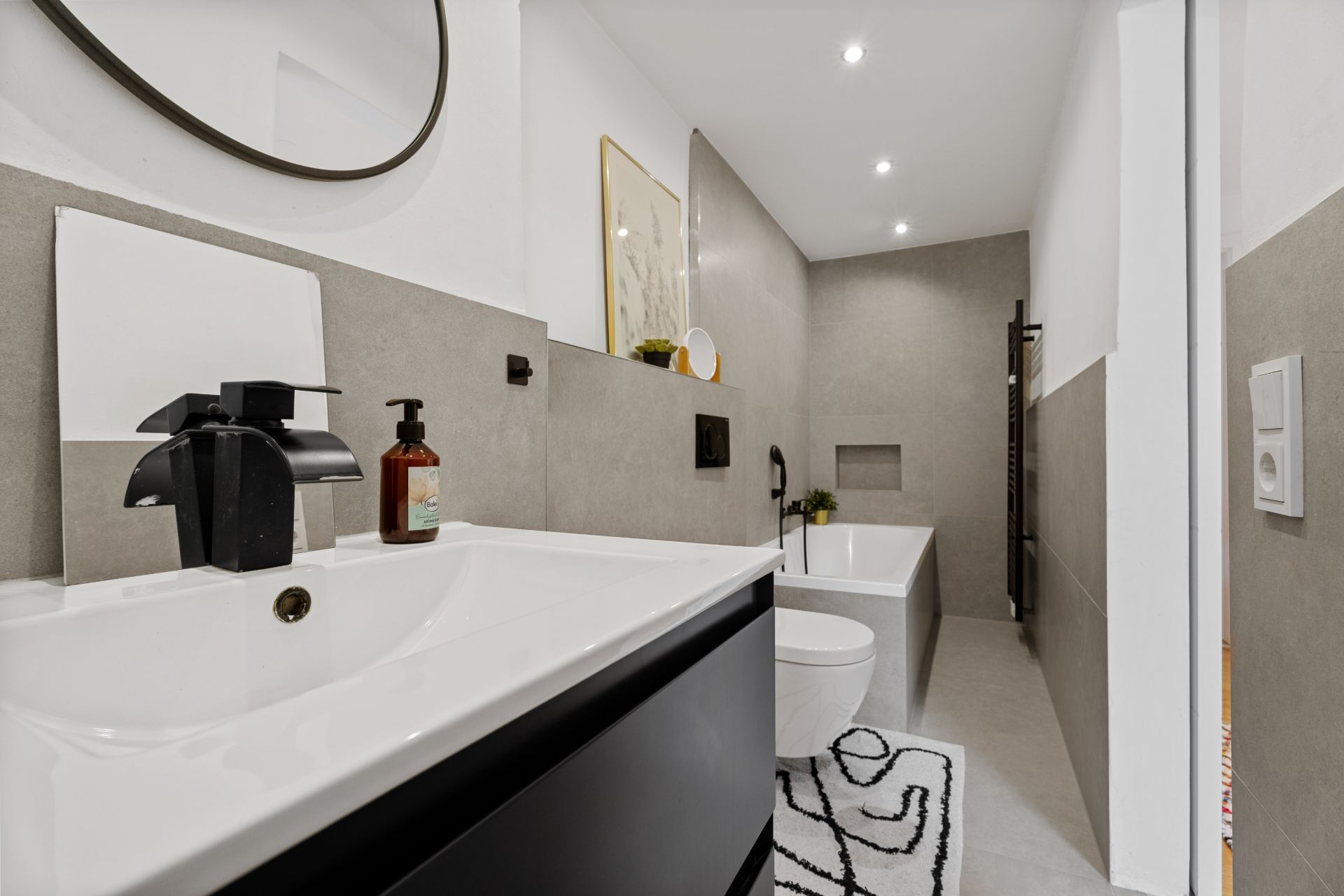 Modernes Badezimmer mit Waschbecken, Spiegel, Toilette und Badewanne, helle Wände und schlichte Deko.