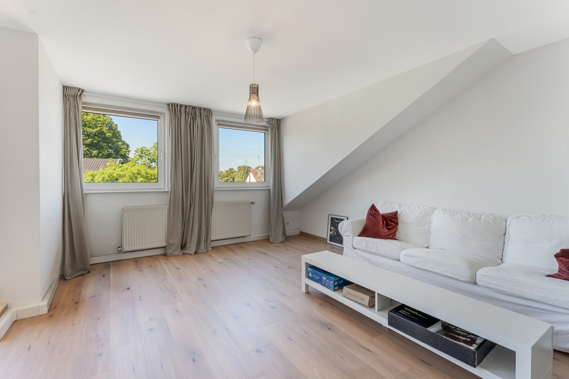 Helles Wohnzimmer mit Holzfußboden, weißem Sofa und zwei Fenstern mit grauen Vorhängen.