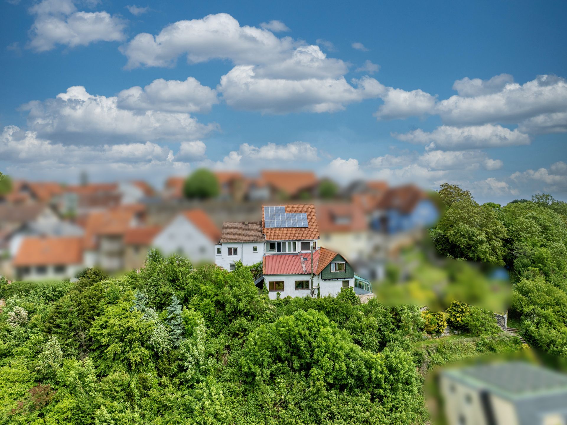 Haus mit Solarpanel auf dem Dach, umgeben von Bäumen und weiteren Häusern im Hintergrund.