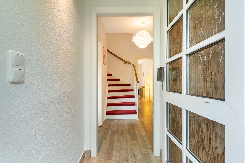 Eingangsbereich mit offener Tür, Holzfußboden und Treppe mit rotem Teppich.