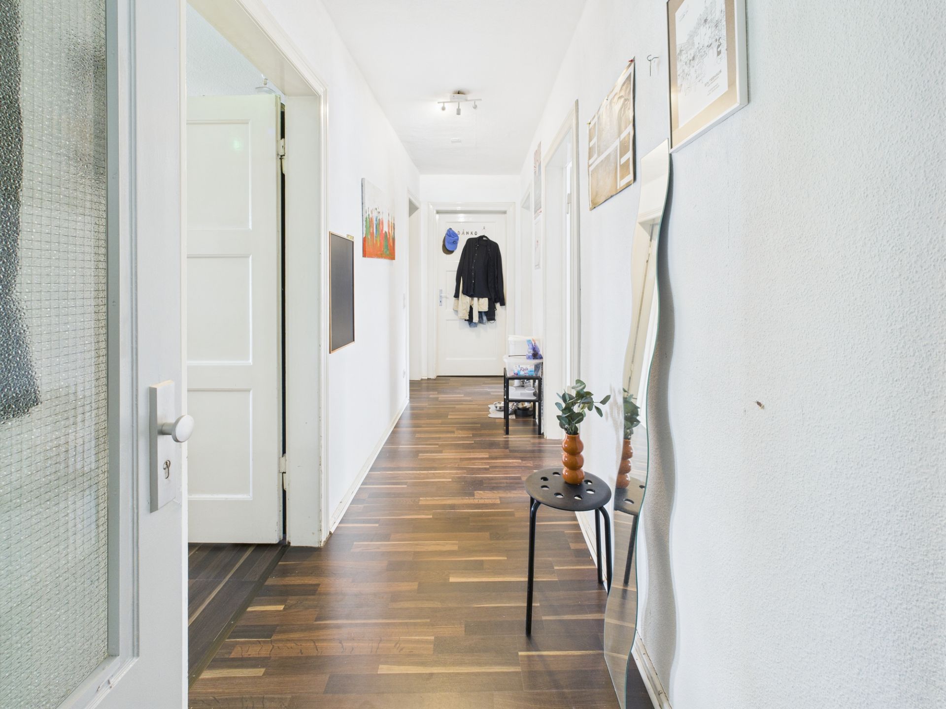 Heller Flur mit Holzfußboden, Spiegel und Tisch mit Vase, Türen und Garderobe sichtbar.
