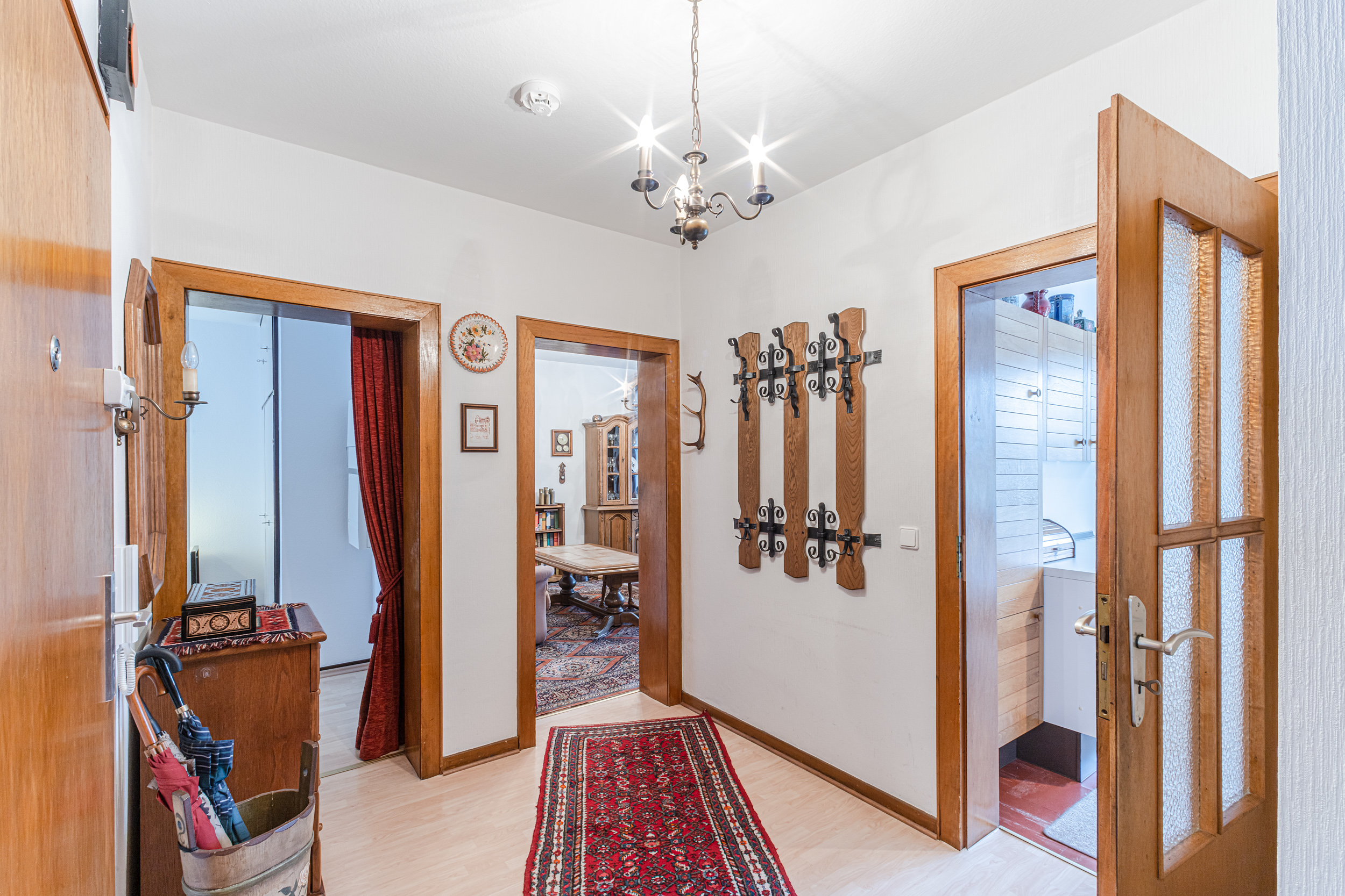 Flur mit Holztüren, Garderobe, Teppich und Blick in angrenzende Zimmer einer Wohnung.