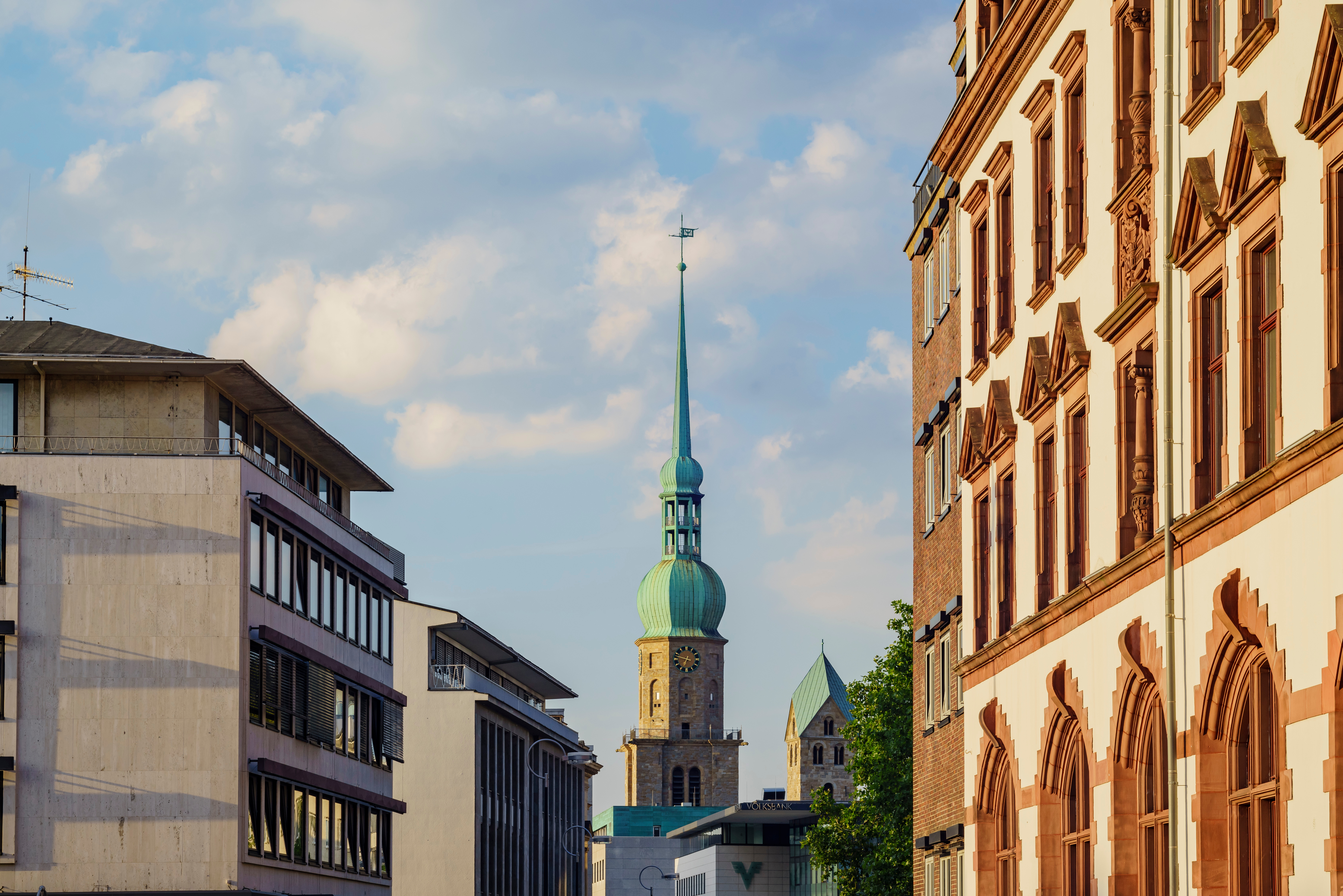 Blick auf eine Straße mit modernen und historischen Gebäuden, Kirchturm im Hintergrund.